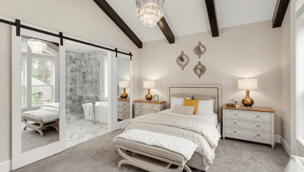 A rustic master bedroom with vaulted wood beams and a white sliding barn door leading to an attached bathroom.