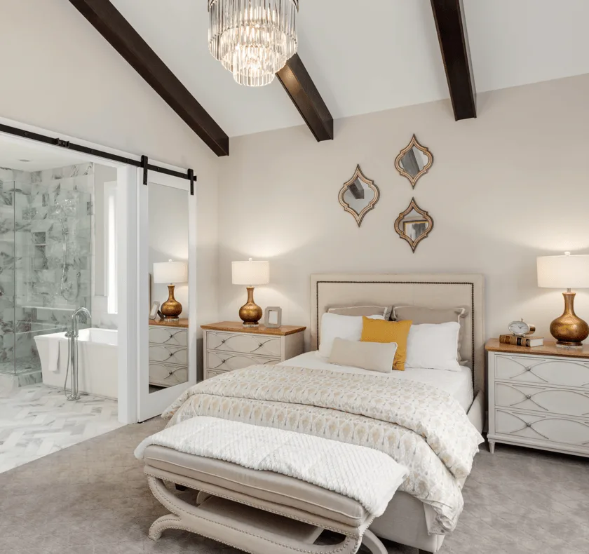 A rustic master bedroom with vaulted wood beams and a white sliding barn door leading to an attached bathroom.