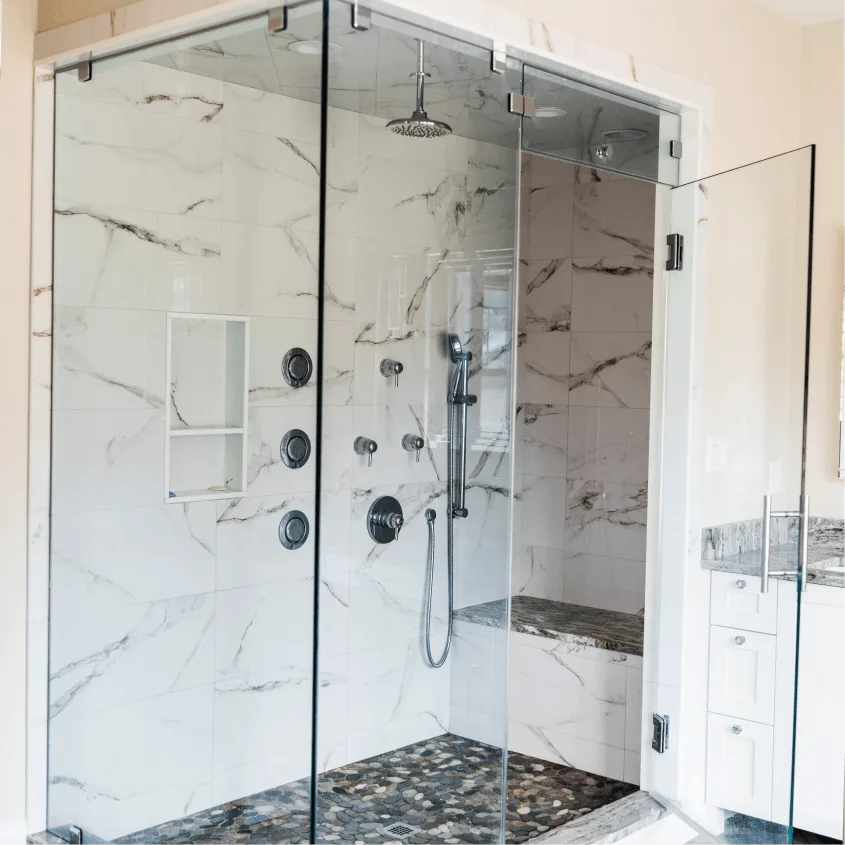 A spacious walk-in shower with floor-to-ceiling white marble tile and multiple modern chrome body jets.