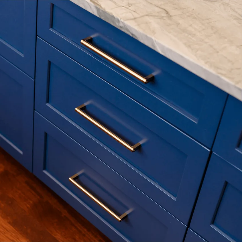 A close-up shot of deep blue kitchen or bathroom drawers with sleek, long gold or brass handles, topped with a light stone countertop.