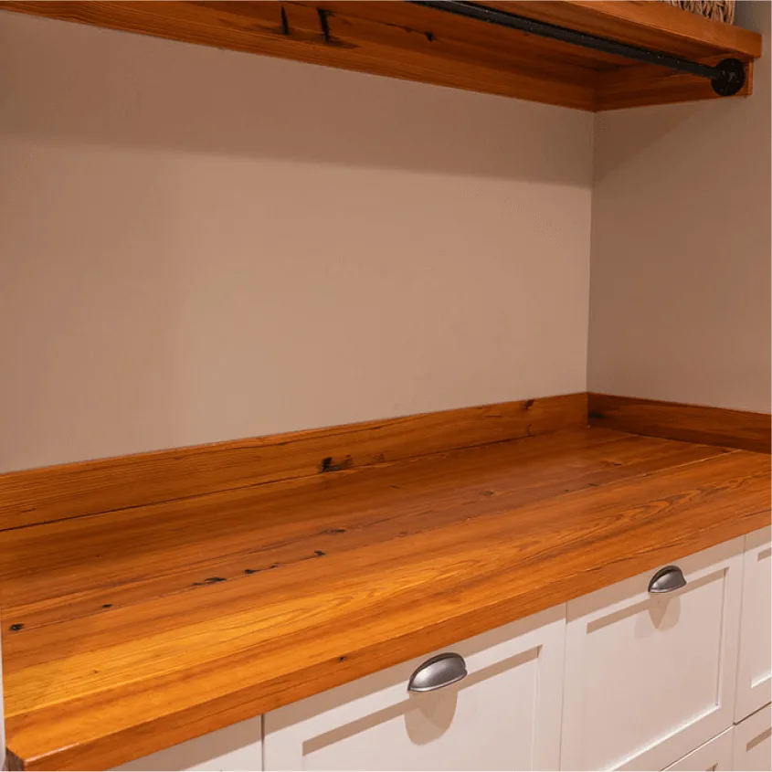 A close-up shot of a built-in home counter space featuring white cabinetry beneath a warm, polished wood countertop.